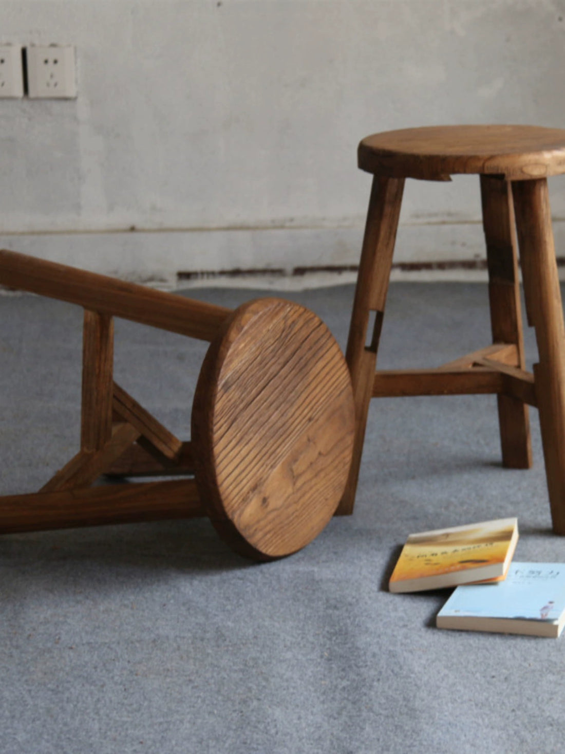 Rustic wooden stool, round top, natural wood finish,  on gray carpet.