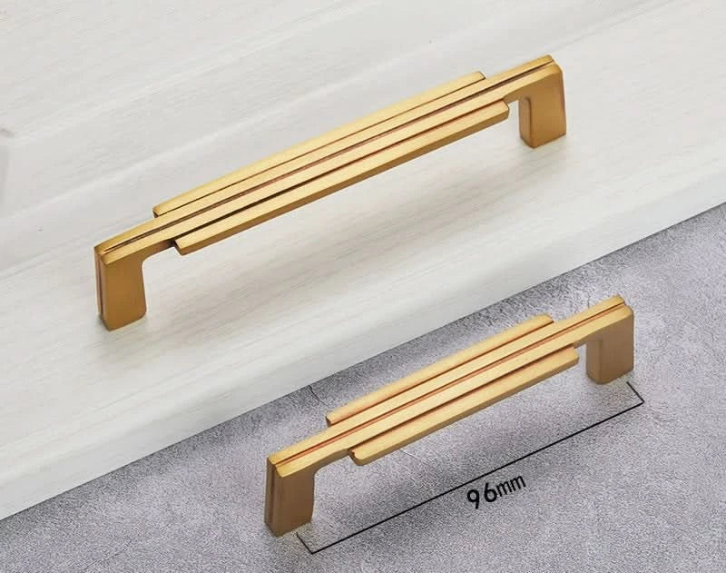 Modern gold geometric cabinet handles on white surface, showing stylish black copper detail.