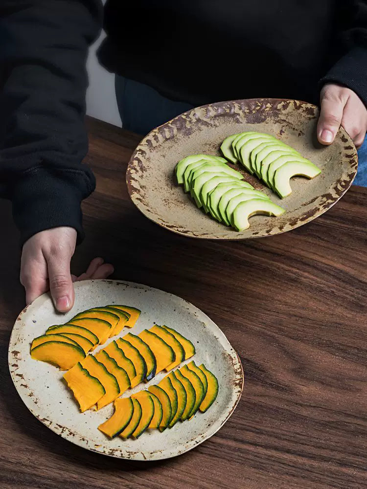 Two hands displaying ceramic plates: one with sliced zucchini and another with sliced cooked pumpkin.