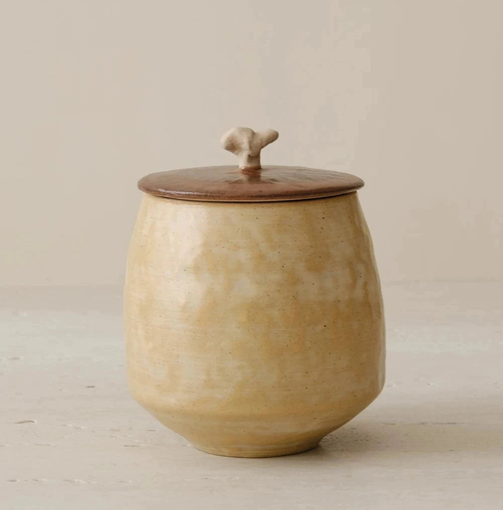 Off-white ceramic storage jar with a natural wooden lid and a unique artisanal finish.