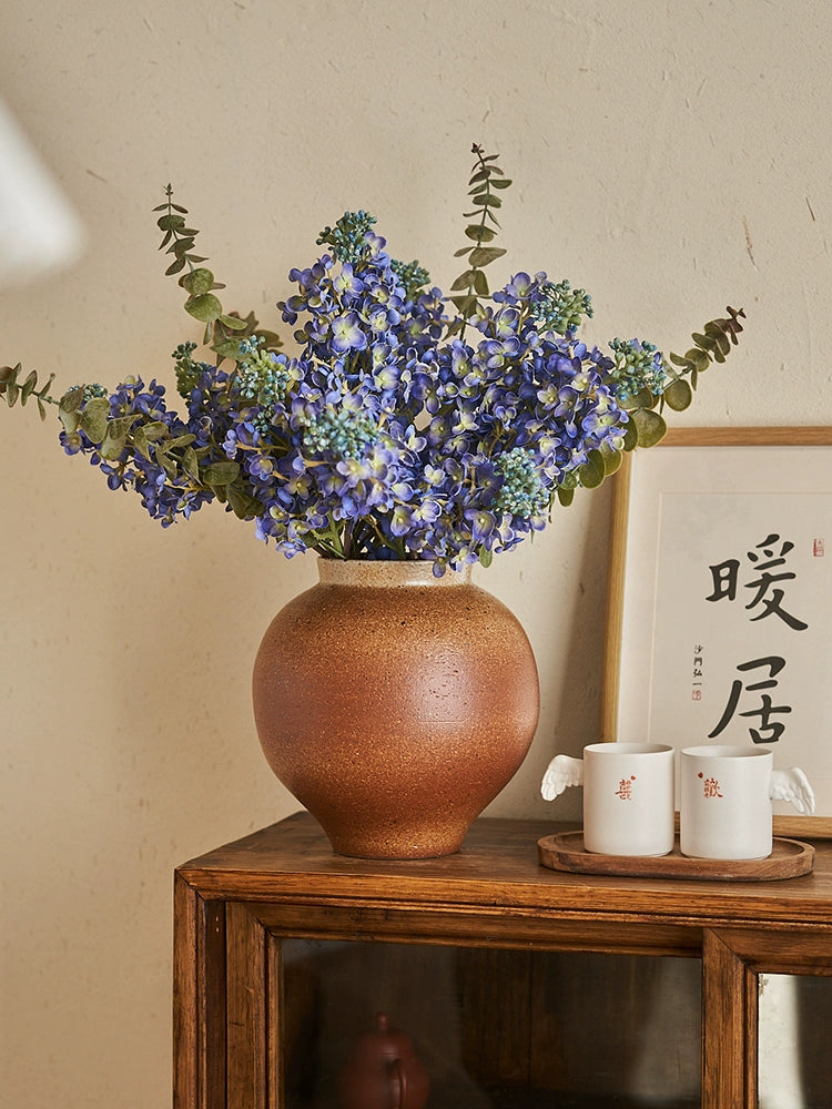 Rustic brown handmade pottery vase, 23cm tall, filled with a bouquet of small purple flowers and eucalyptus.  Unique texture and glaze.