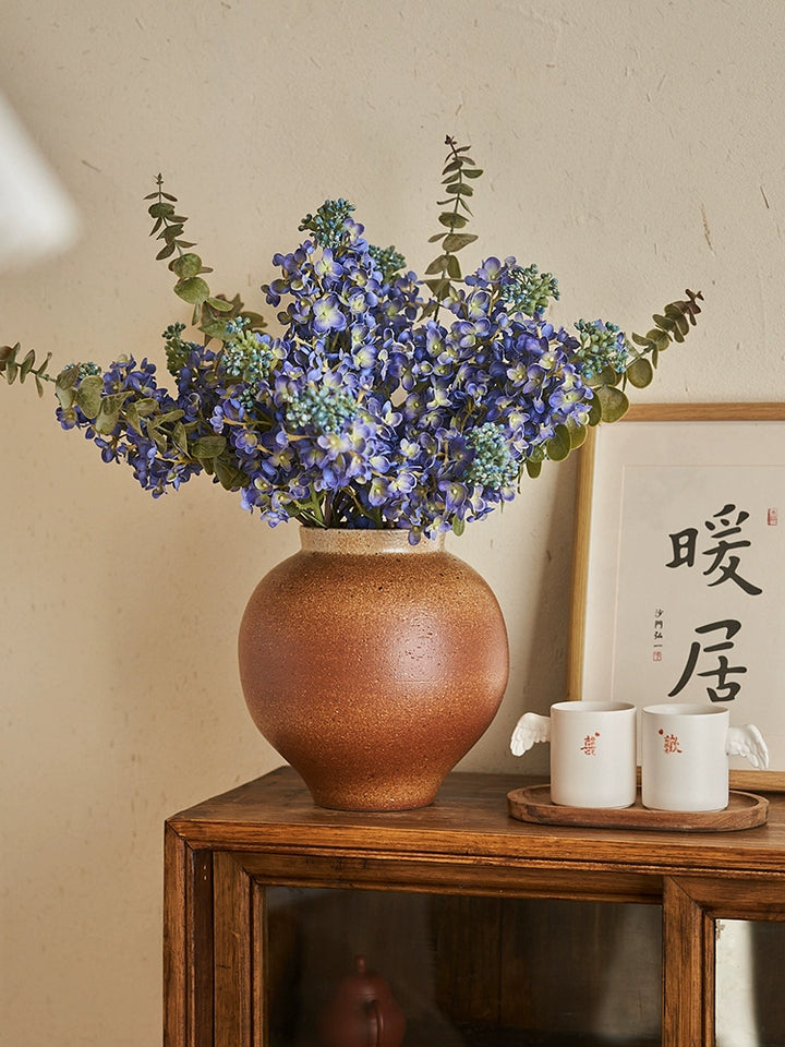 Rustic brown handmade pottery vase, 23cm tall, filled with a bouquet of small purple flowers and eucalyptus.  Unique texture and glaze.