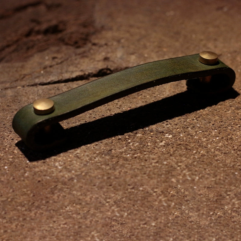 Green leather drawer pulls with brass accents, rustic cabinet handles for wooden furniture.