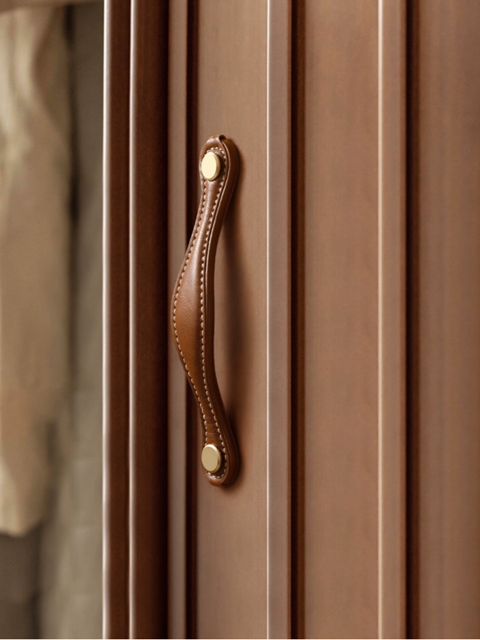 Brown leather-wrapped drawer pull with brass accents on a light brown wooden cabinet.
