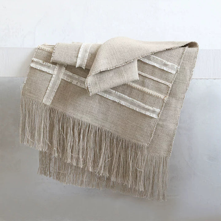 Beige linen table runner with woven design and fringe.