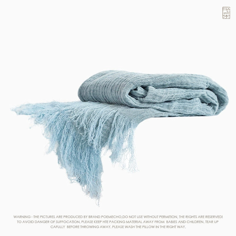 Light-blue linen throw blanket with textured fabric and frayed fringes.  Rustic style.