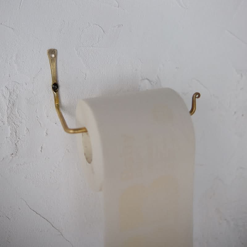 Gold toilet paper holder with a textured white wall background.