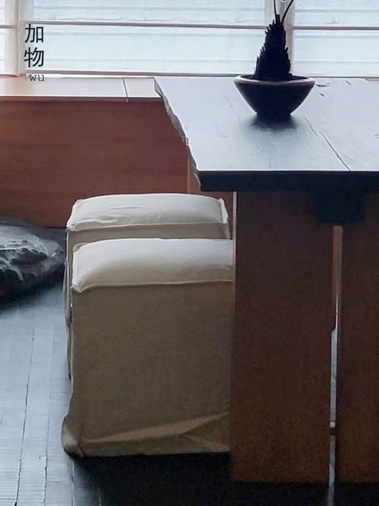 Two beige linen square footstools, modern minimalist style, on a dark wooden floor.