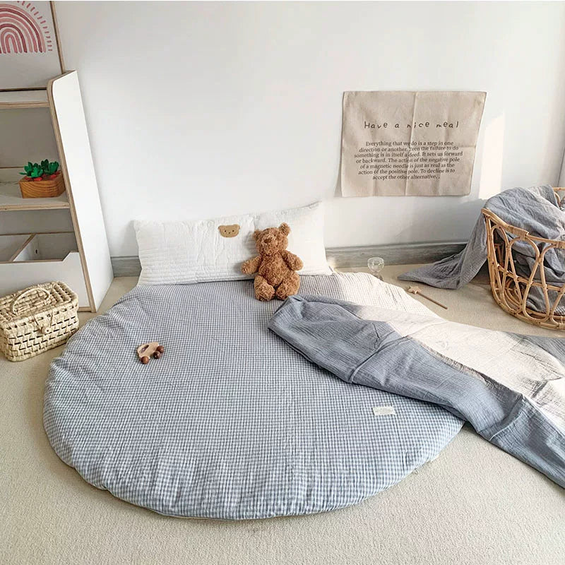 Round light blue and white gingham play mat next to a teddy bear and blue blanket.
