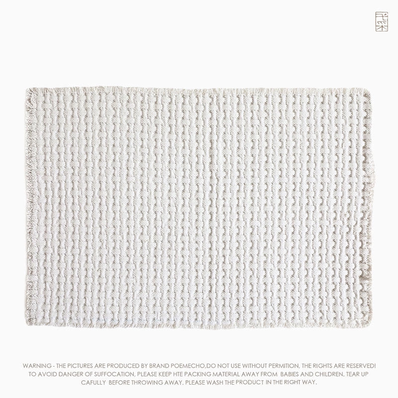 Beige woven cotton throw blanket, textured with a repeating pattern of small bumps, creating a soft, cozy feel.  Fringed edges.