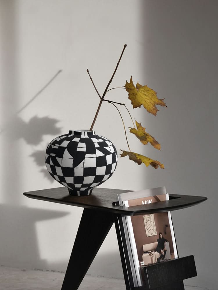Black and white checkered ceramic vase with dried leaves on a modern black side table.