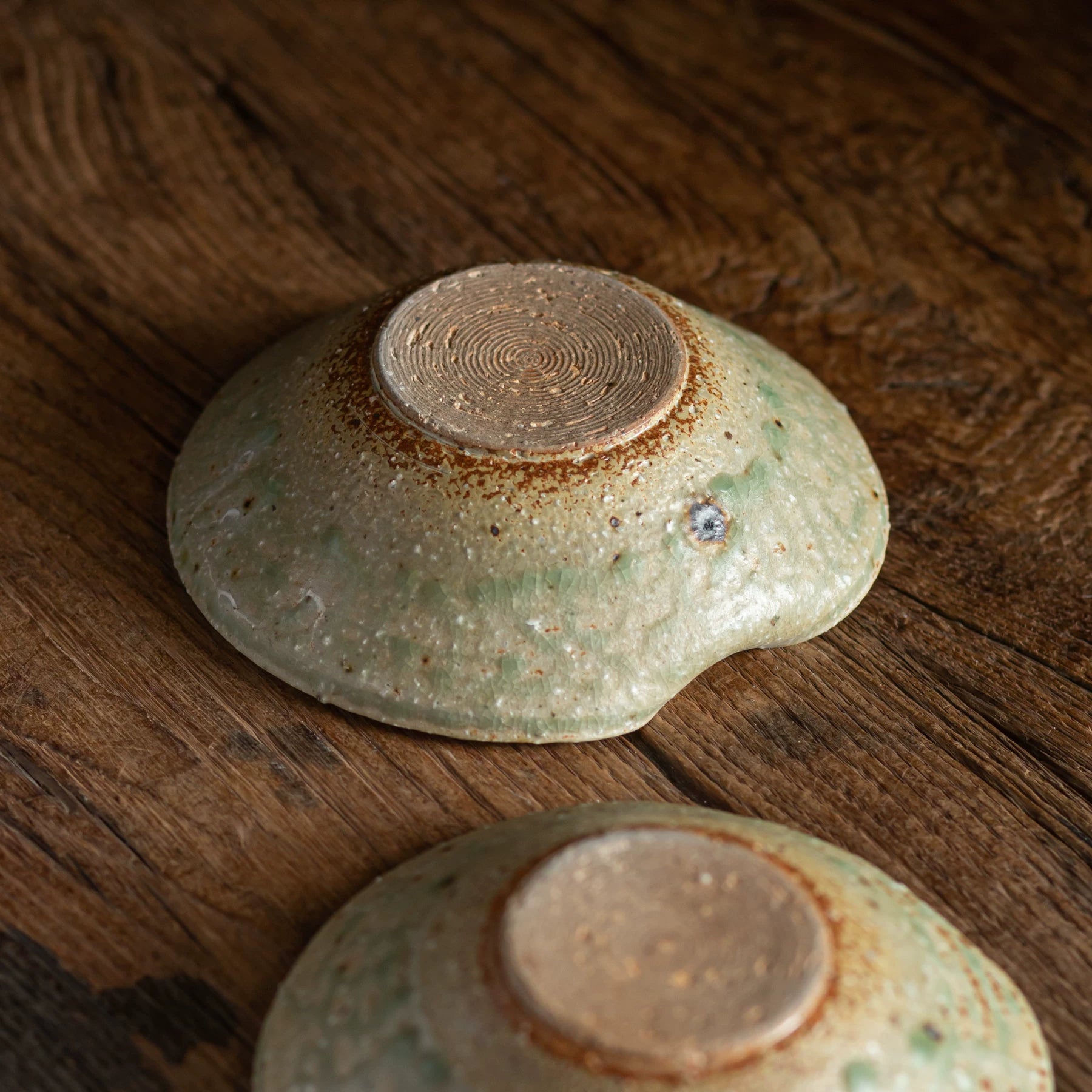 Bottom view of two heart-shaped ceramic bowls showing the unglazed, concentric circle foot rings on wood.