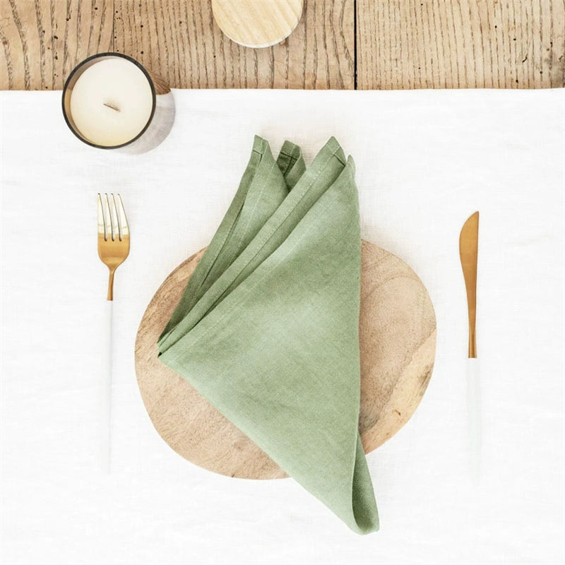 Sage green Elegant Linen Table Napkins, knotted, set of 4, on a placemat with gold flatware.