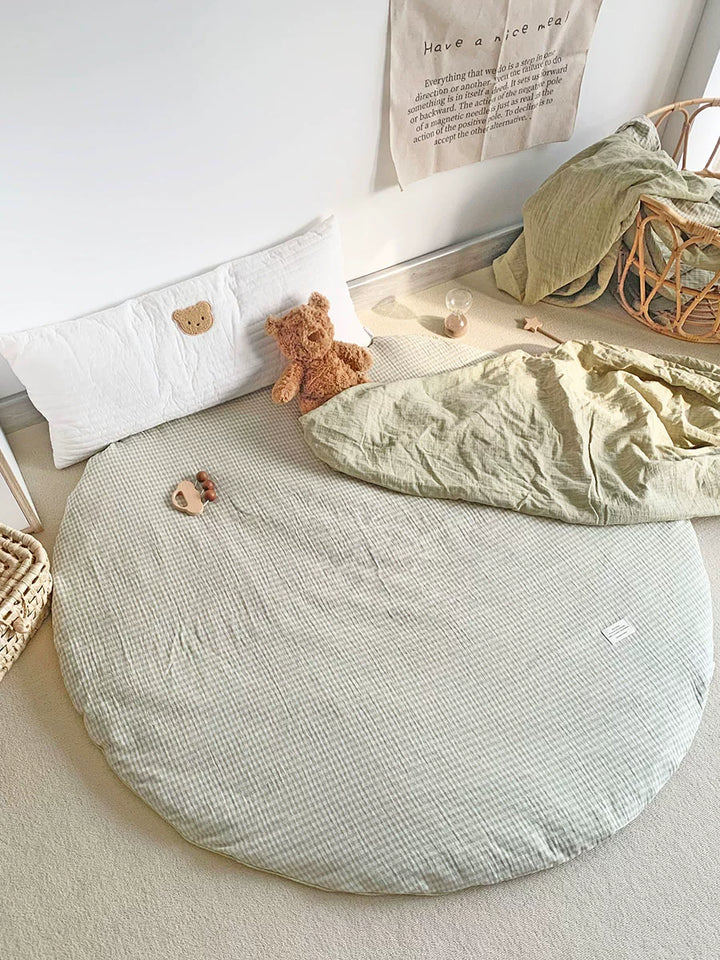 Round baby play mat in pale sage green and white gingham check pattern with teddy bear.
