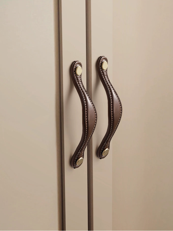 Two brown leather-wrapped cabinet handles mounted on light beige cabinets.  Gold colored hardware.  Modern farmhouse style.
