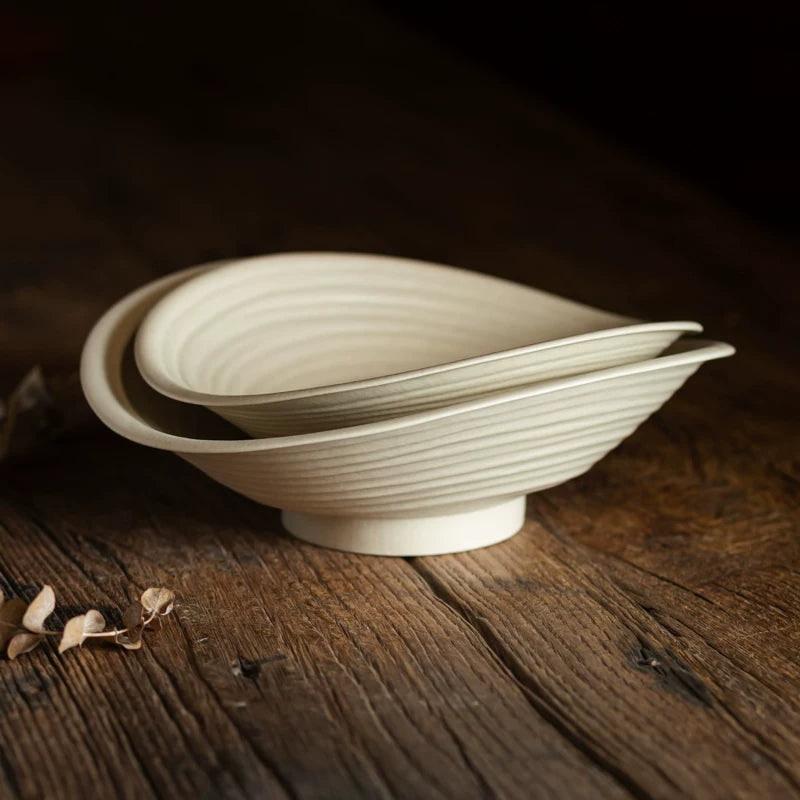 Two stacked ceramic bowls featuring fine concentric ridging on the exterior, on a dark wood surface.
