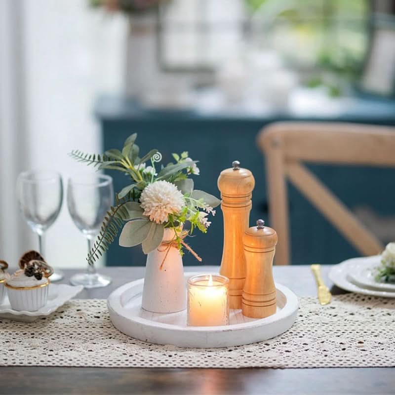 White wooden tray decorative with flowers, candle, and salt/pepper grinders on a table.