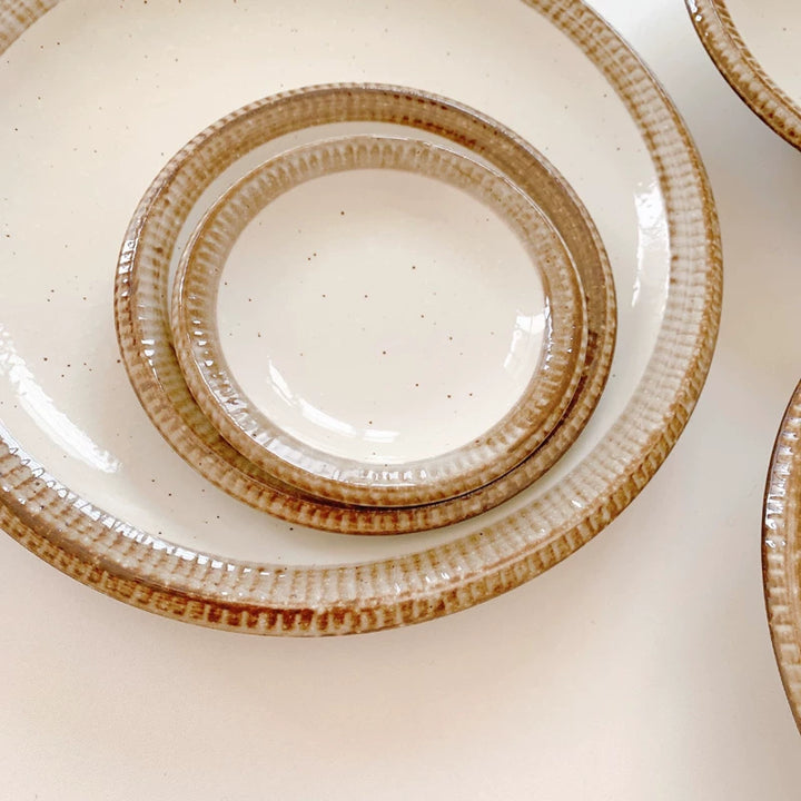 Close-up of two nested ceramic plates featuring a speckled white center and wide, grooved brown border.