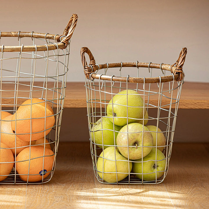 Two rustic wire baskets with woven handles.  One filled with oranges, the other with green apples.  Silver wire, light brown handles.