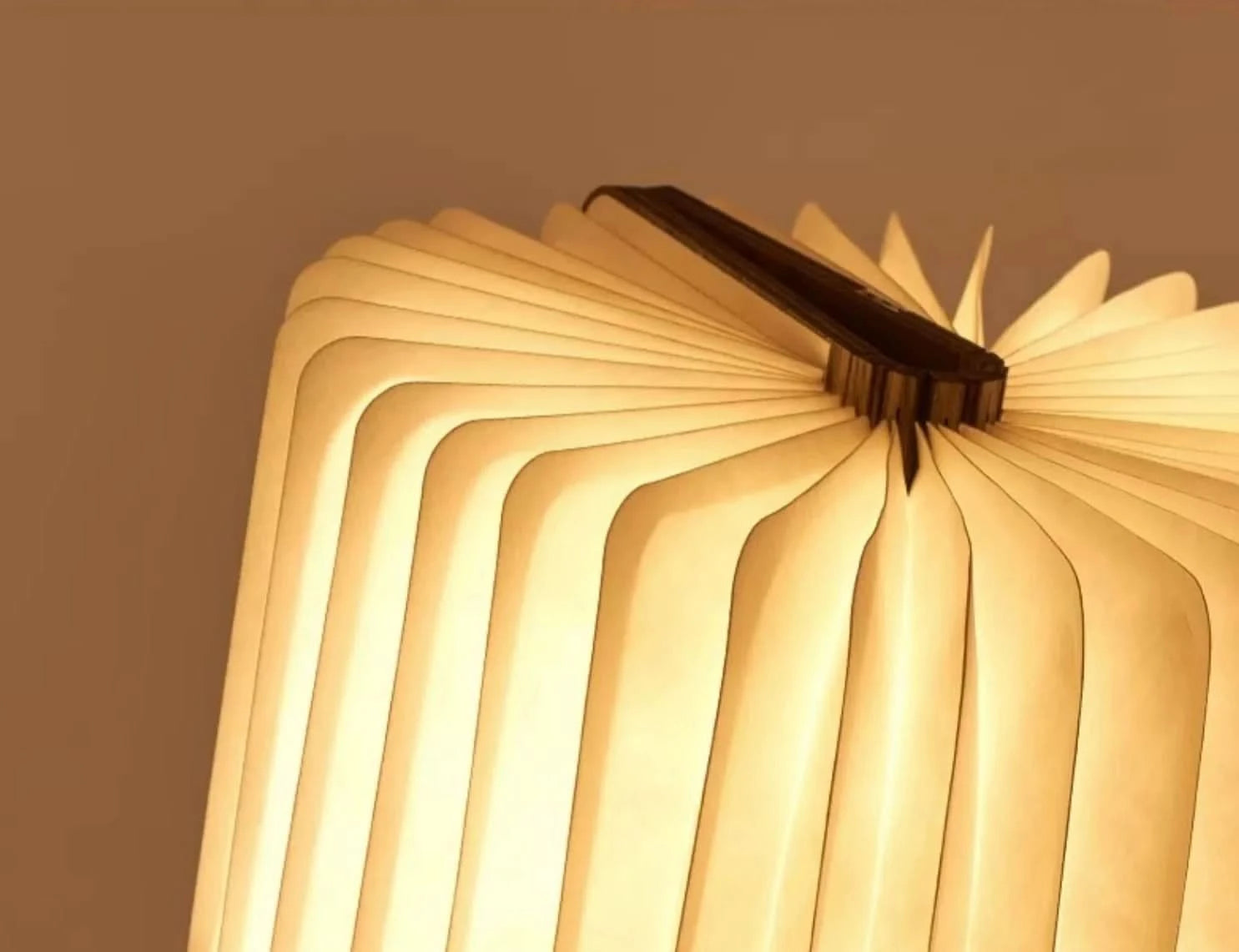 Glowing folding portable paper lamp with a dark spine, emitting warm light.