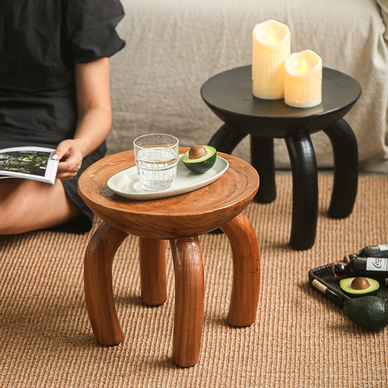 Ethnic style wooden side table: round coffee table with curved legs, brown wood, on rug.