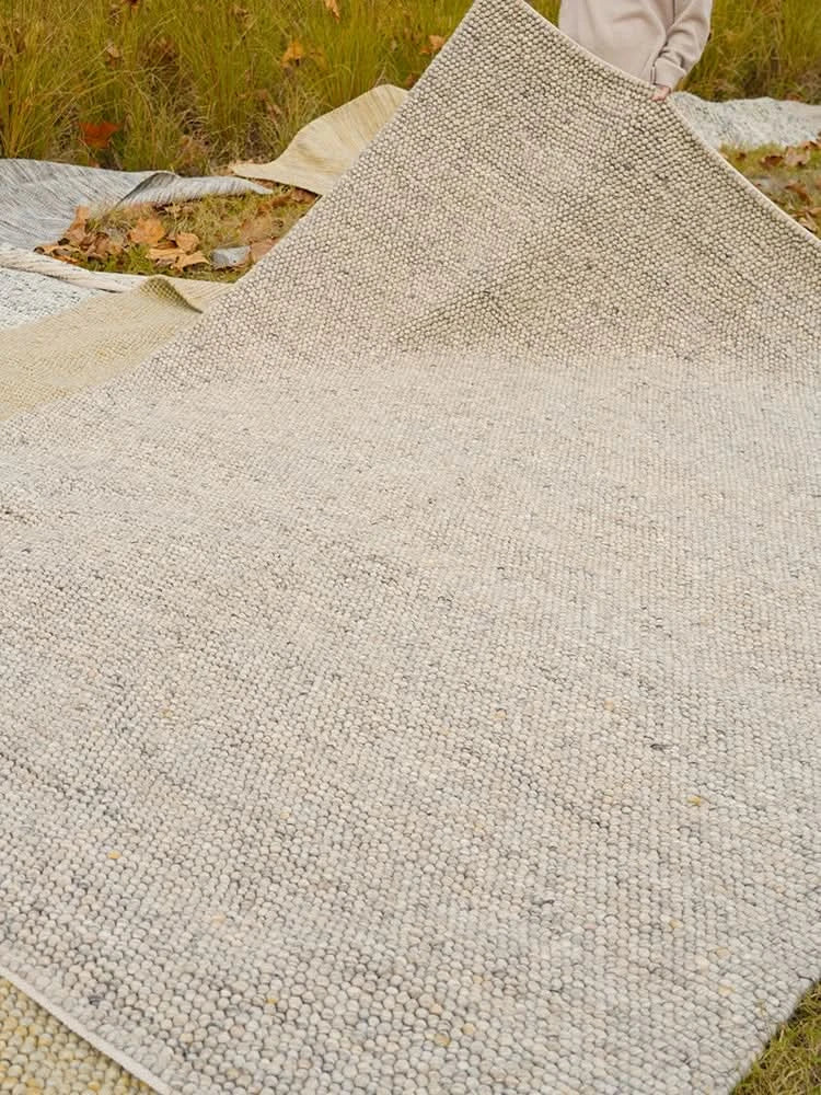 Handmade wool rug in light neutral tones, displaying cozy texture on grass.