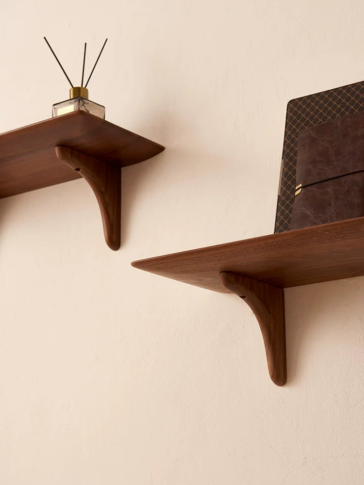 Close-up of dark wood floating shelf with curved brackets holding a diffuser and book.