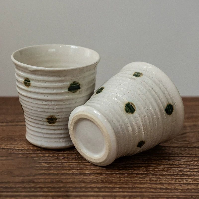 Two white ceramic tea cups on a wooden surface; one upright, one tilted to show the unglazed base with green spots.