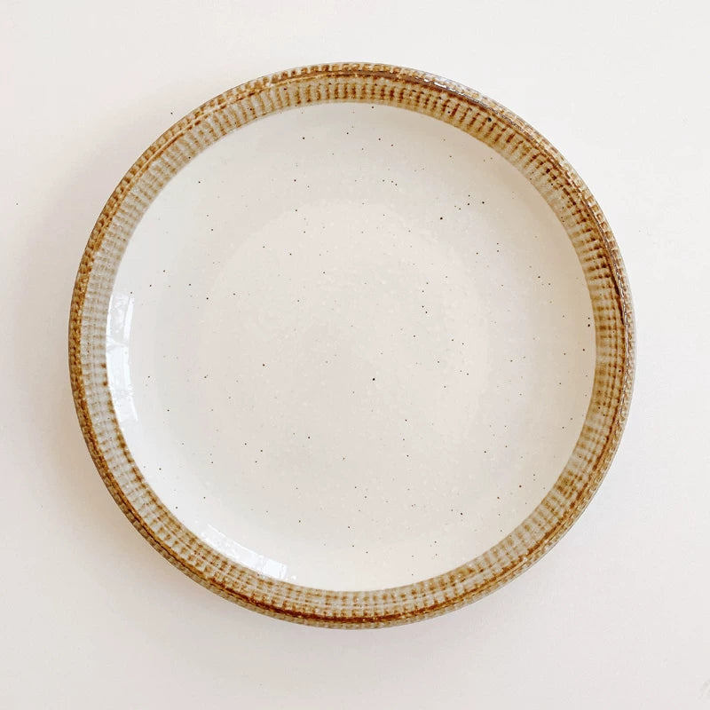 Large flat ceramic dinner plate with a speckled white center and a wide, textured brown rim.