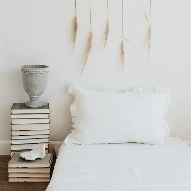 Elegant white linen pillow cases with frills, on a bed.