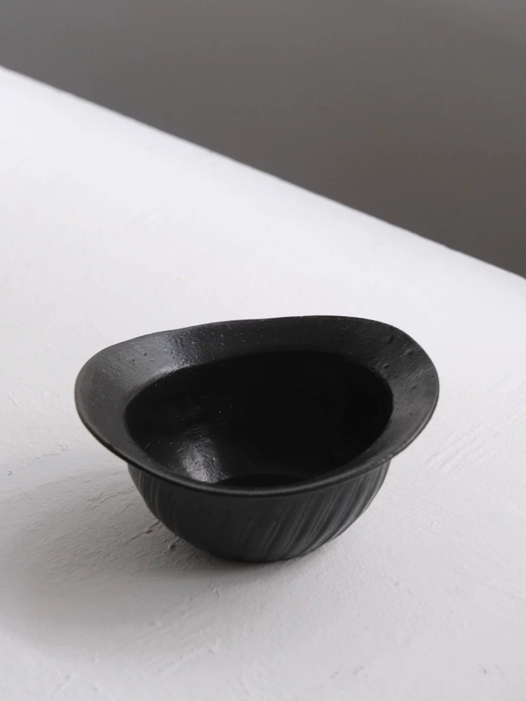 Small black ceramic bowl with fluted sides on a white surface