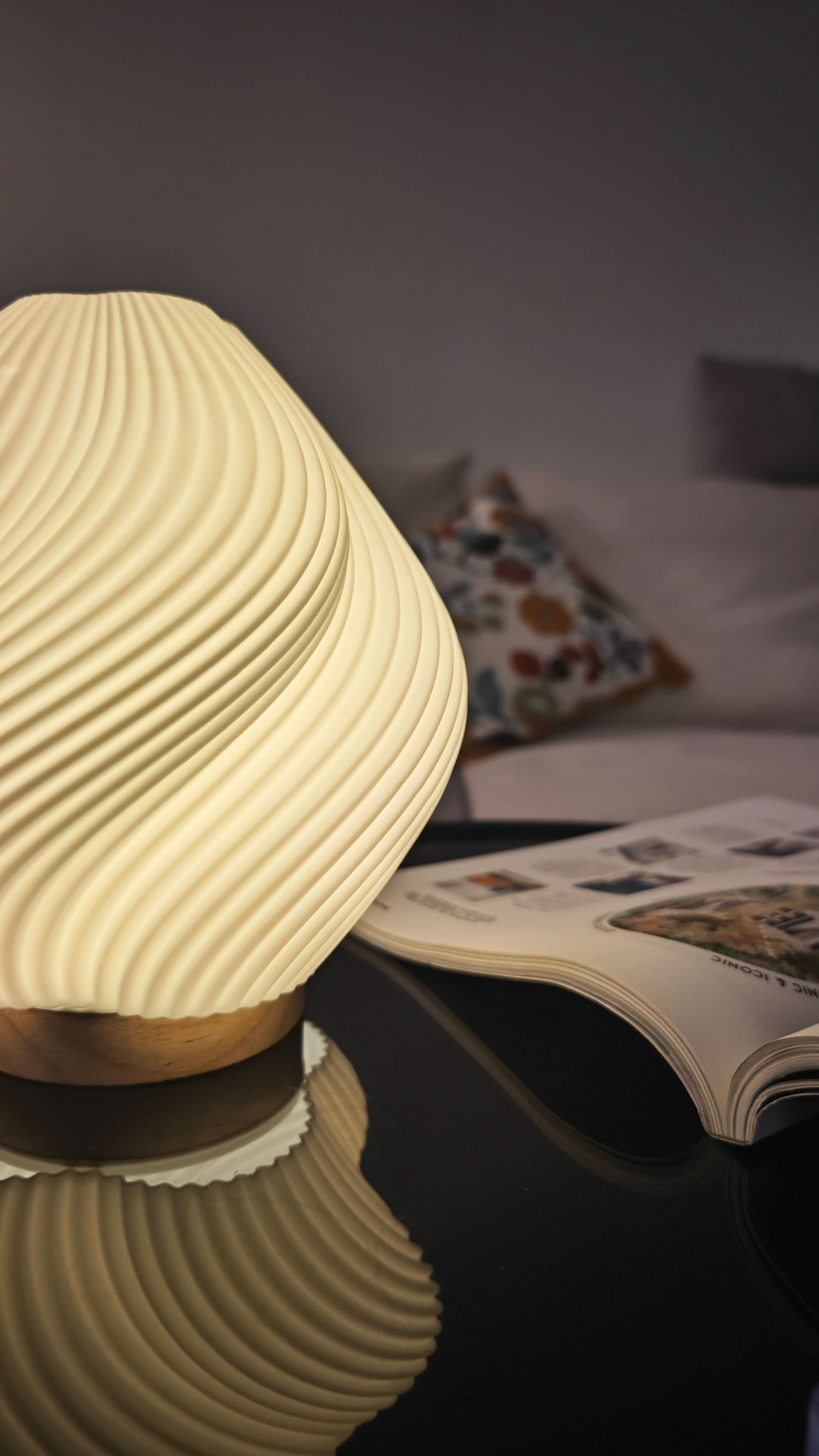 Whimsical Wave Table Lamp with wooden base, on black surface with open magazine and pillows.