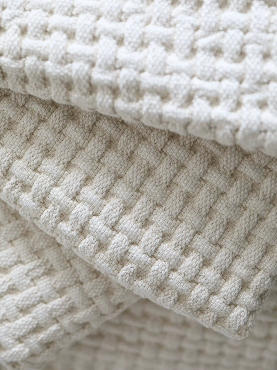 Beige woven cotton throw blanket, close-up view of textured weave.