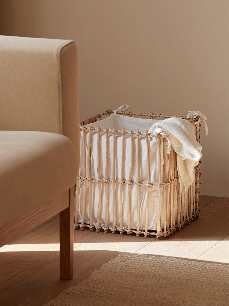 Natural rattan storage basket with white liner and draped blanket on wooden floor.
