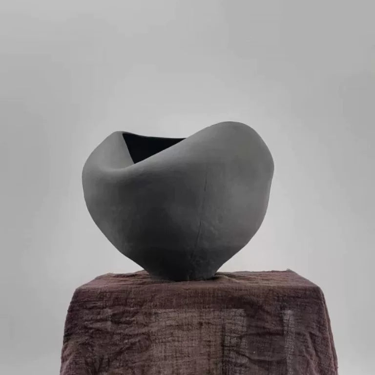 A handmade ceramic vase with a sculptural, folded design and a textured matte finish.