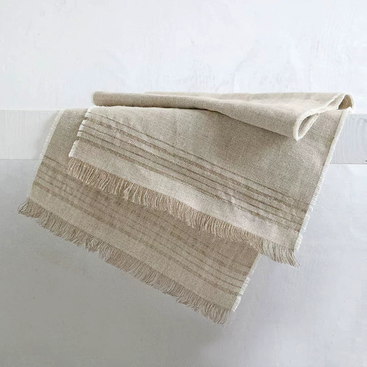 Natural beige linen table runner with fringe and horizontal stripes.