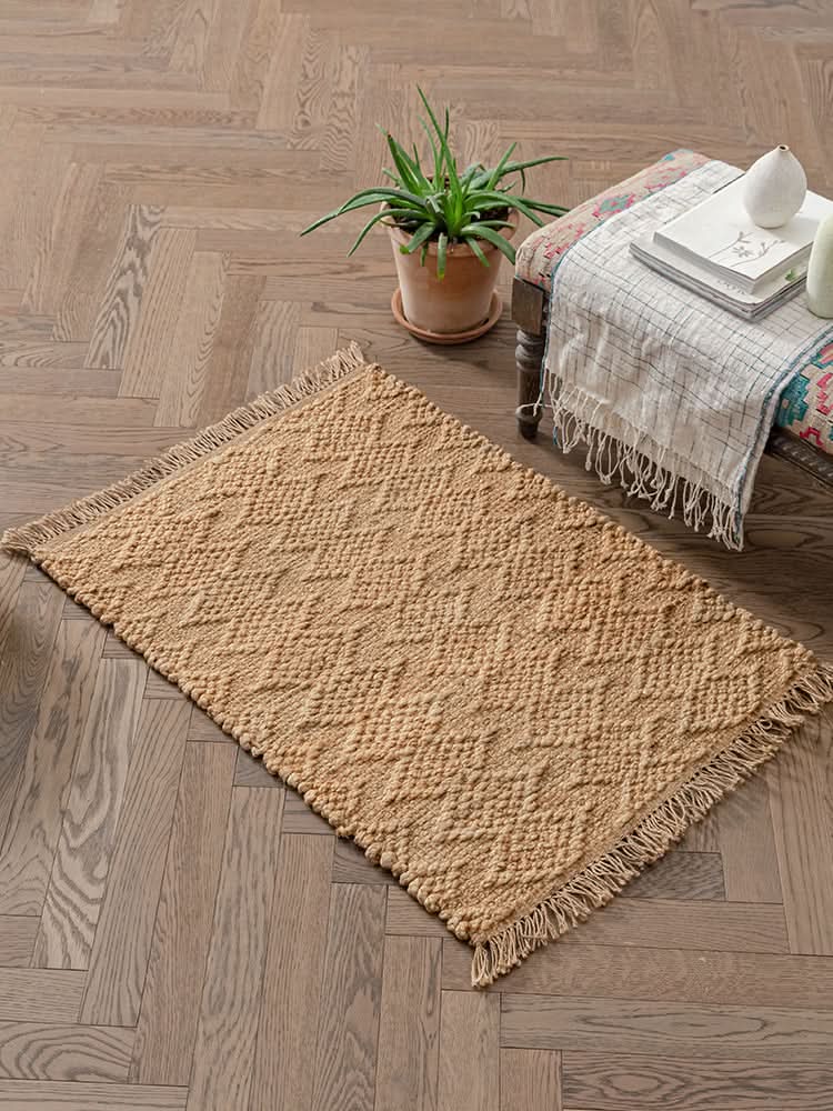 Textured woven natural area rug in a warm, neutral tone with fringed edges on a wood floor.