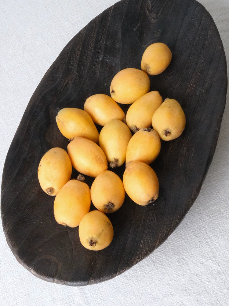 Several ripe loquats in a dark wooden oval platter.