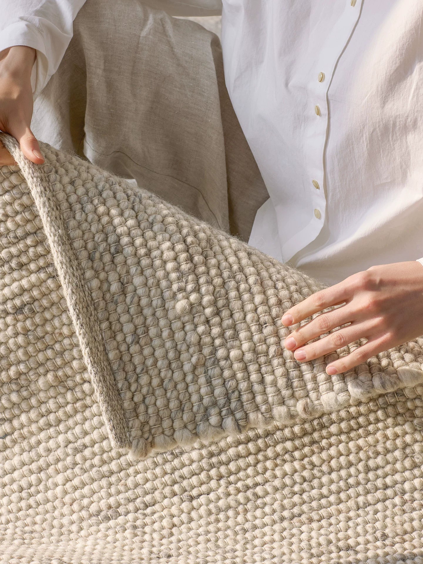 Person folding cream wool rug showing thickness and texture