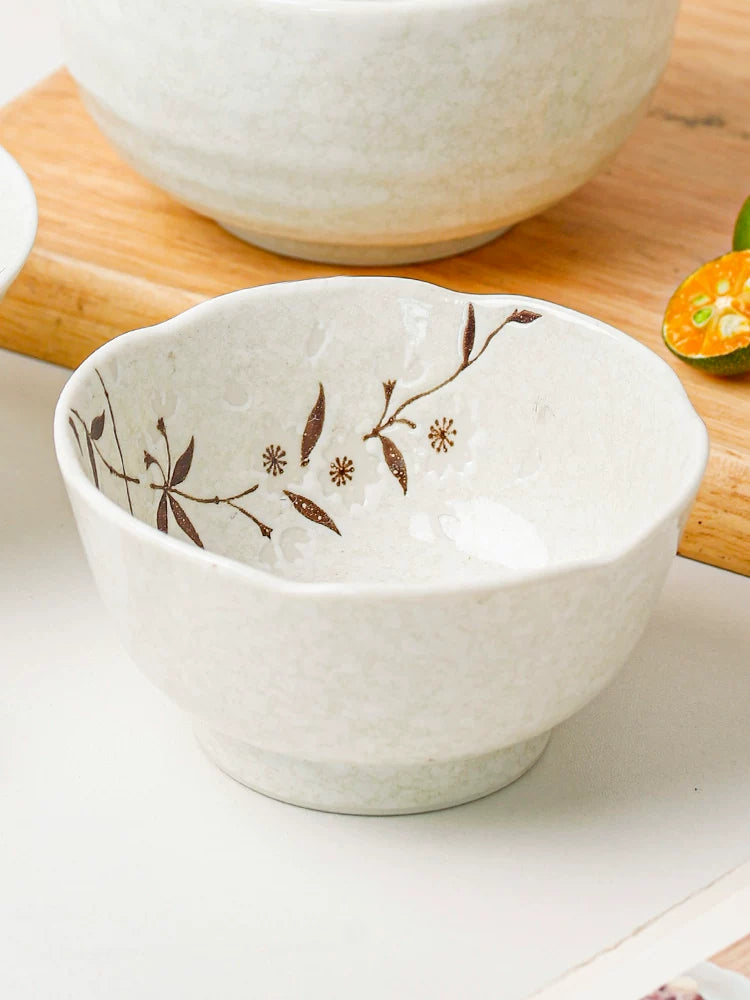 Close-up of a white ceramic bowl with brown cherry blossom pattern on a wooden board with citrus fruits.