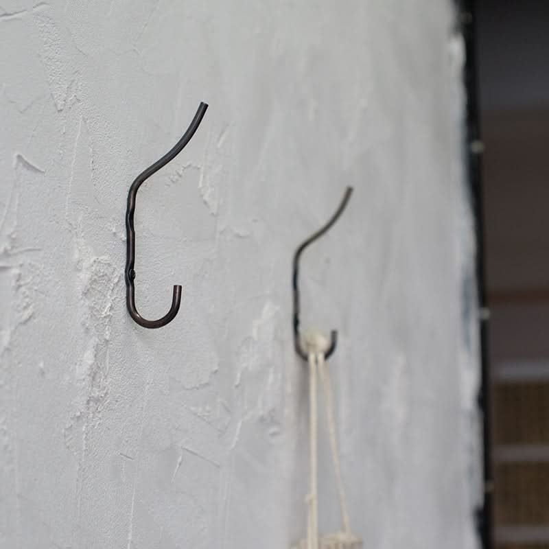 Hand-forged iron wall hooks with rustic texture on a white wall.