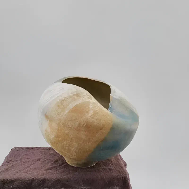 A textured ceramic vase with an asymmetrical, folded sculptural design in a neutral beige tone.