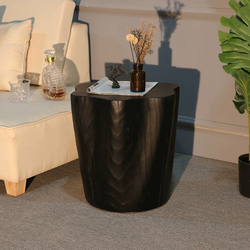 Black natural wood log side table, rustic coffee table on gray carpet with couch and decor.