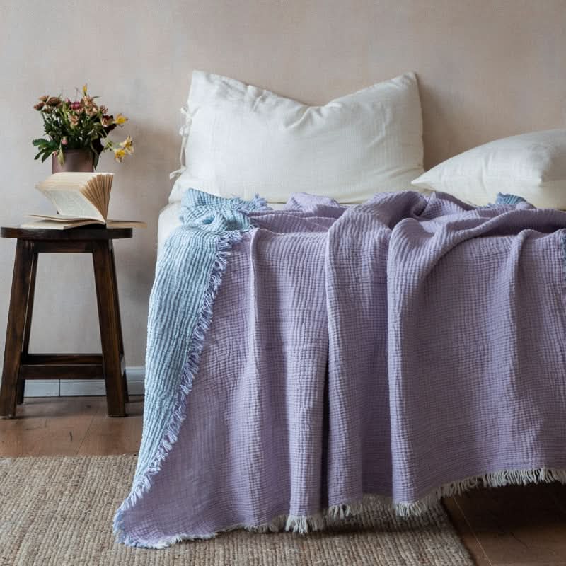 Purple and blue crinkled cotton throw blanket with fringe on a bed.