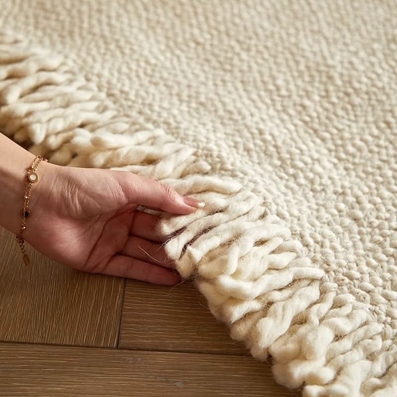 Close-up of hand touching cream braided wool rug on wood floor.