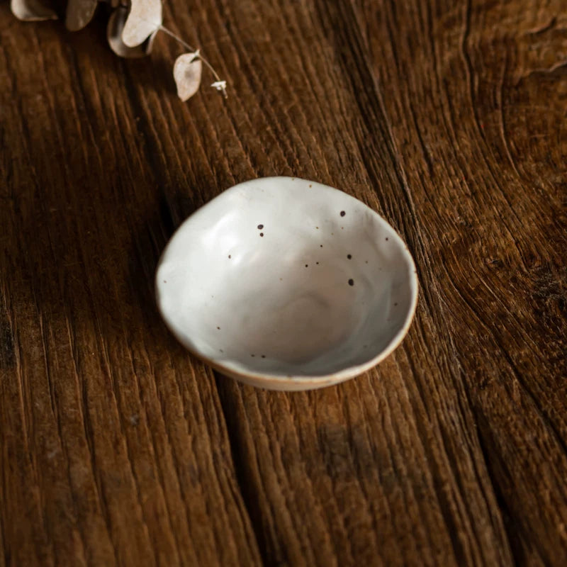 Close-up of a tiny, deep, speckled white ceramic dipping bowl held in a person's hand.