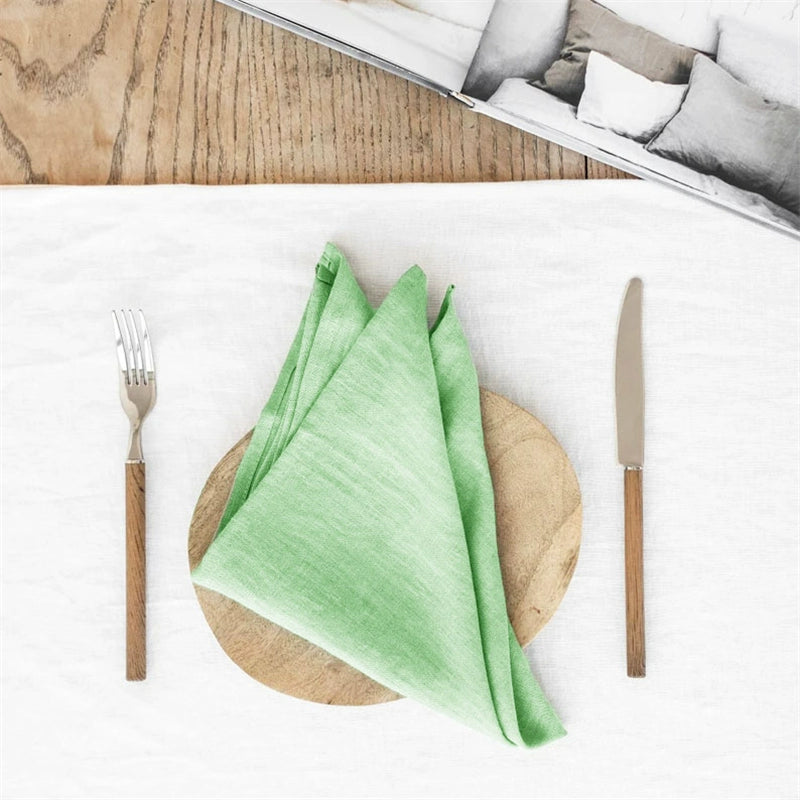 Elegant Linen Table Napkins, set of 4, folded green linen on wooden plate with fork and knife.