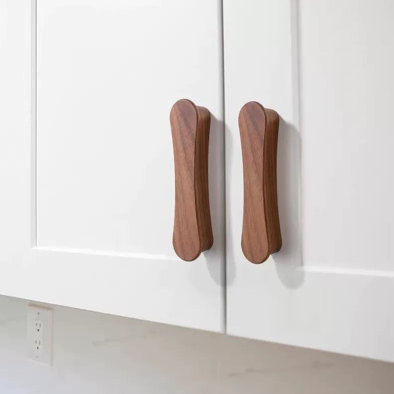 Two streamlined, elongated walnut wood handles mounted vertically on white shaker-style cabinets.