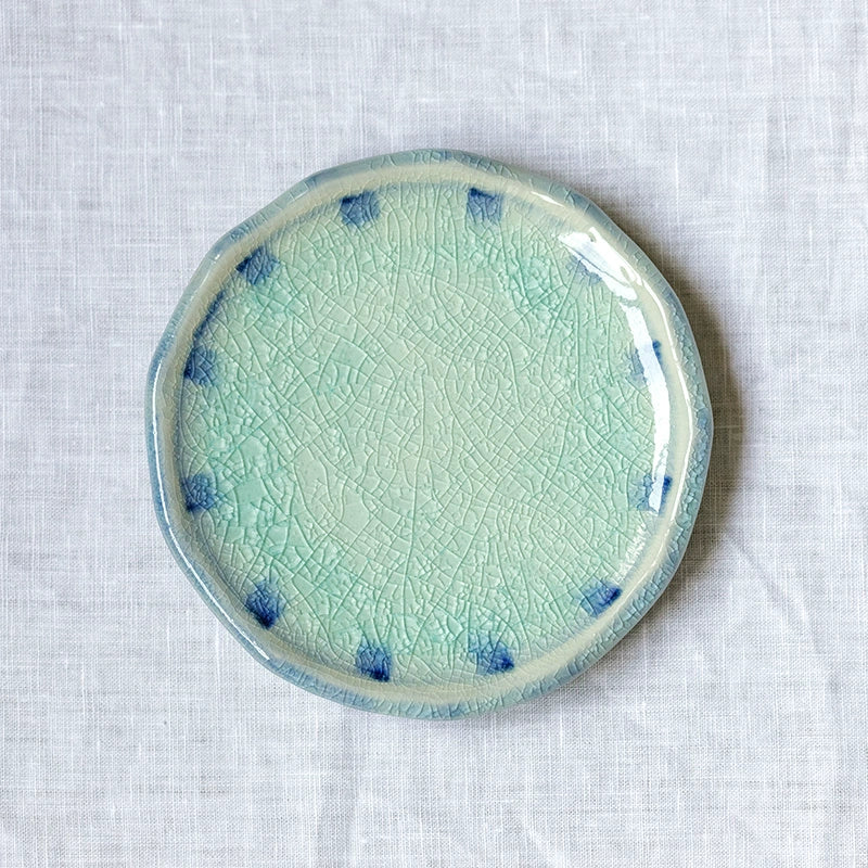 Blue and teal crackle glaze ceramic plate with blue dots on white linen.