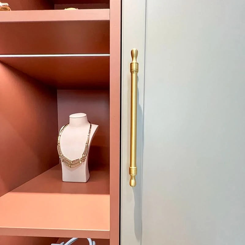 Brass Modern Extended Cabinet Handles on grey door, next to coral shelves and jewelry display.